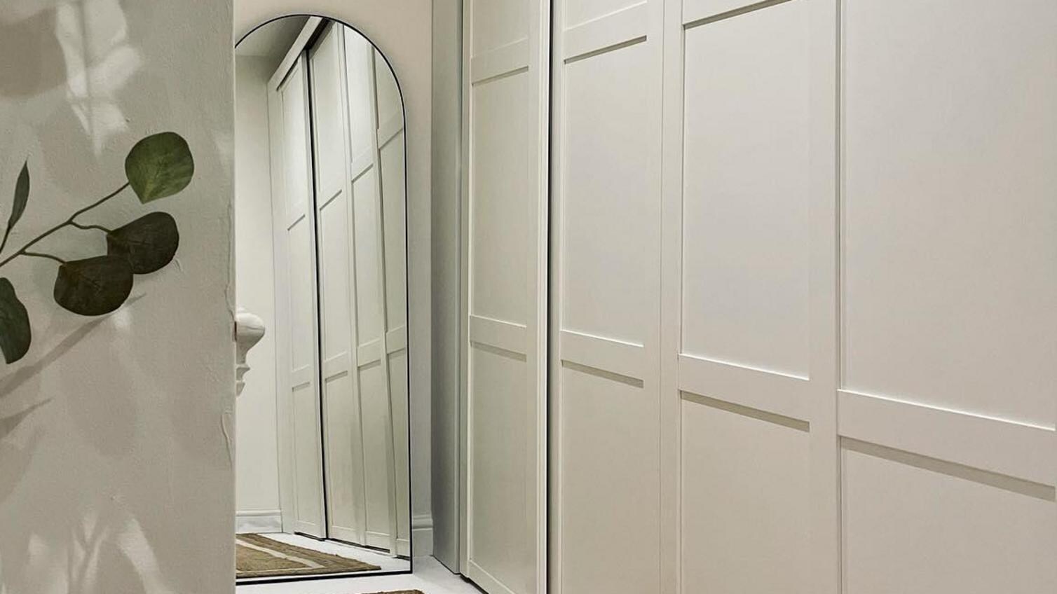 Bedroom home design with a beige sliding wardrobe door, with panelling, a rounded mirror, and a raffia rug.