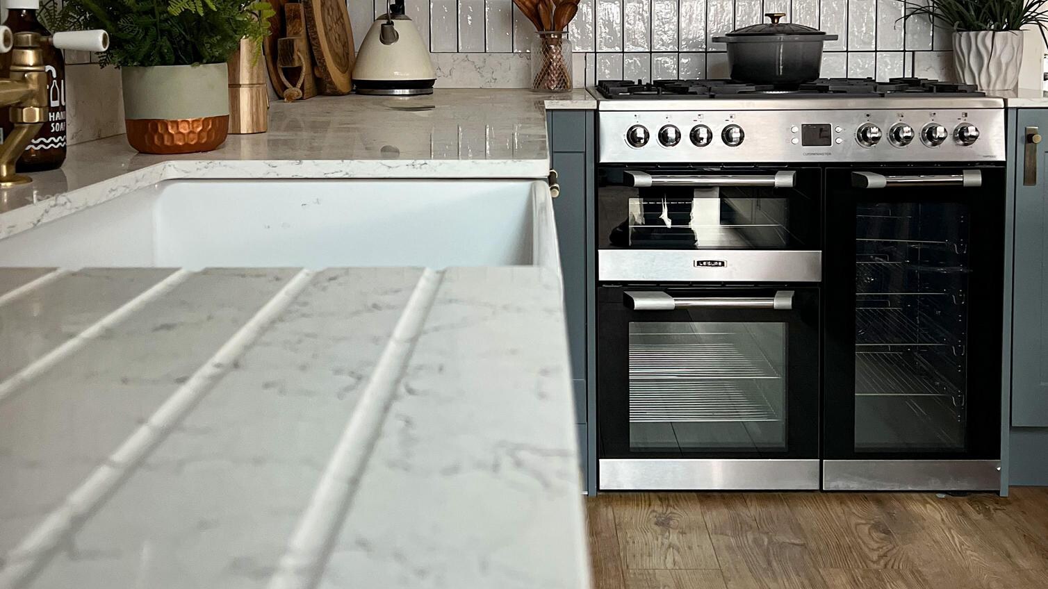 White quartz worktop with a white ceramic sink, dusk blue cabinet doors, and a range cooker and extractor fan.