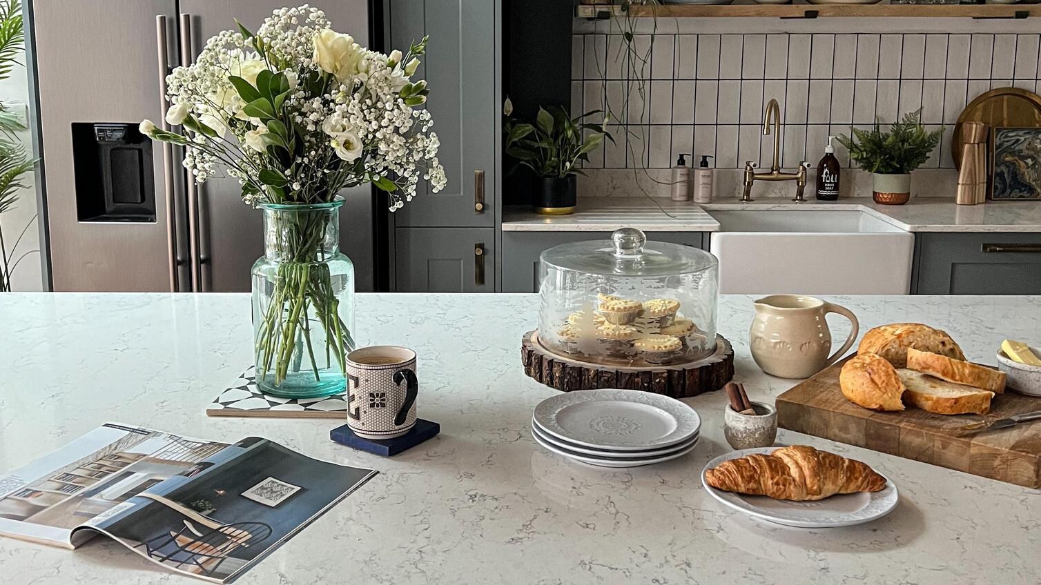 White quartz worktop on a navy shaker kitchen island, showing antique brass cup handles, flowers, and dusk blue wall units.