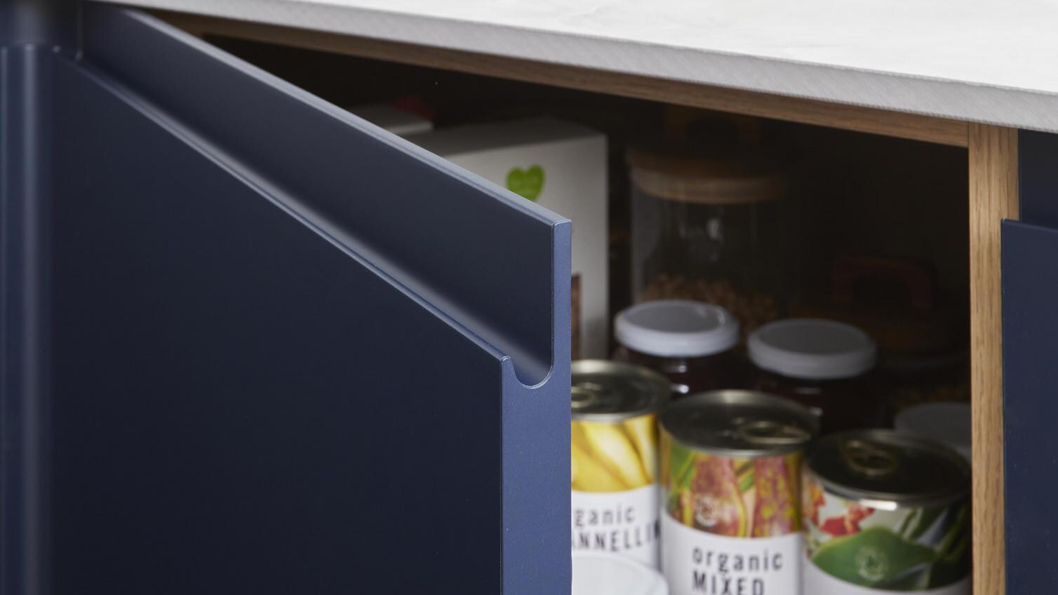 Open kitchen cabinet with built-in storage behind a navy door. Also features a marble-effect laminate worktop.