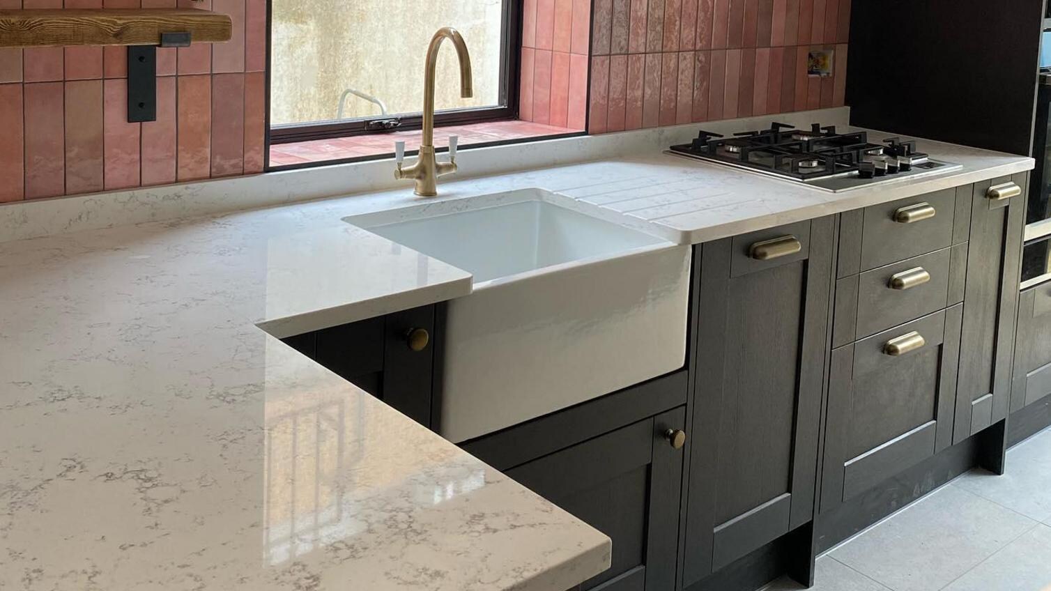 Black shaker kitchen design with a white marble worktop, a white butler sink, gold tap, and pink tiling on the walls.