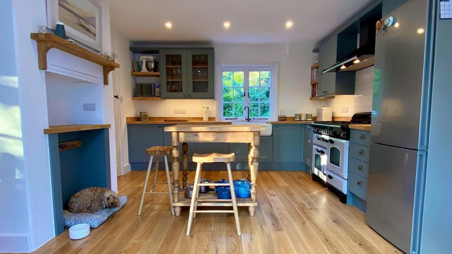 Sage green shaker kitchen idea with an l-shaped layout, a farmhouse style kitchen island with wooden stalls and oak floors.