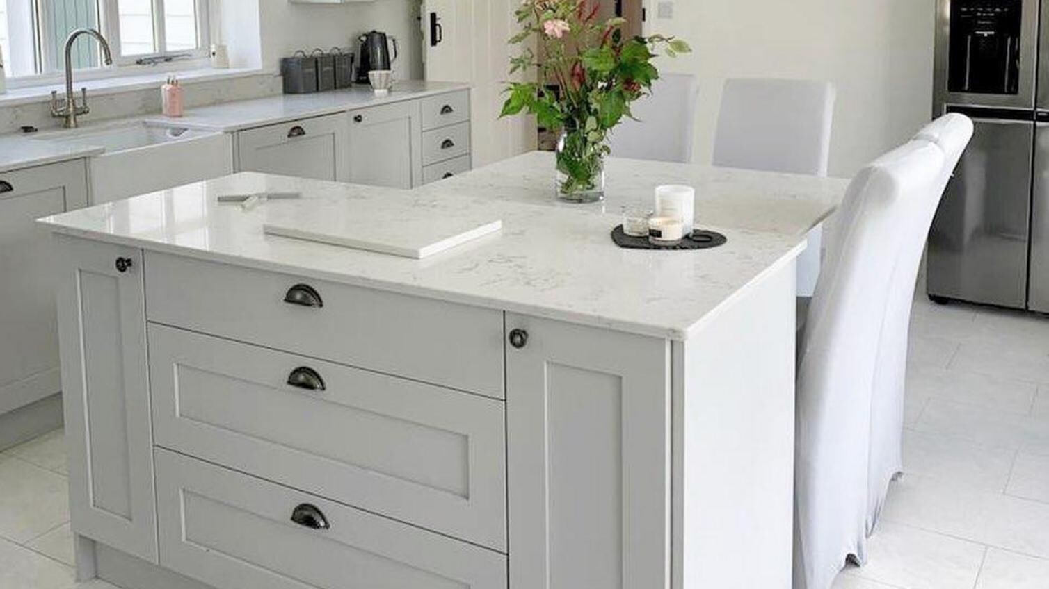 A premium grey kitchen idea featuring solid timber shaker units in dove grey. Includes white worktops, floors, and a sink.