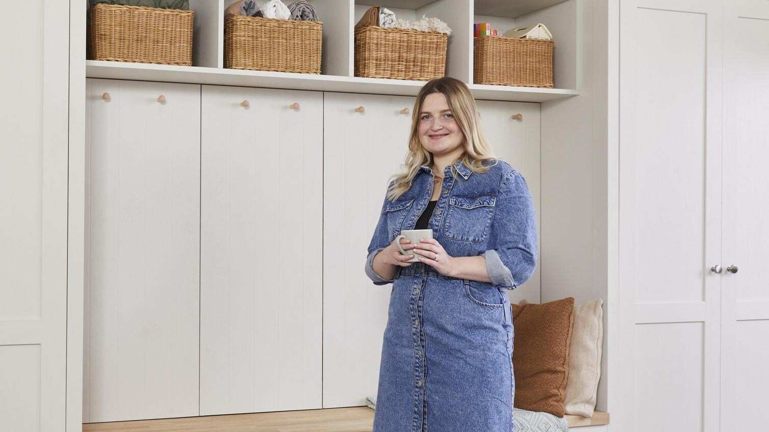 Courtney stood holding a mug, in front of some built in storage units from Howdens