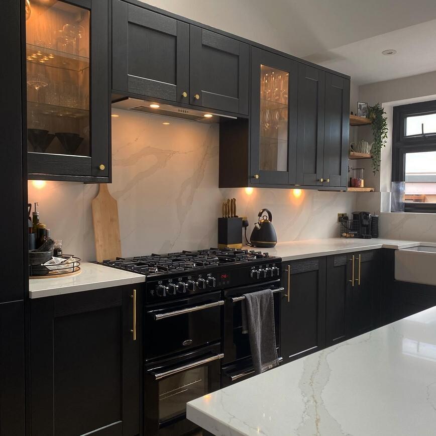 Black shaker style kitchen with glass dresser units, a black range cooker, white marble worktops.