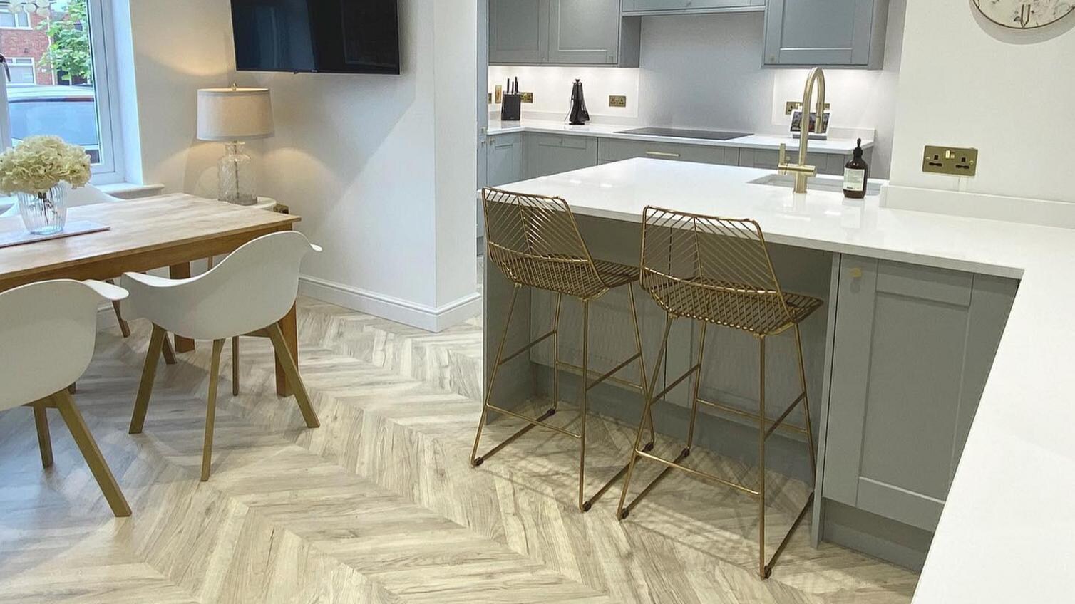 Open plan kitchen and dining room with oak chevron floors, an oak dining table, white chairs, and a grey shaker kitchen.