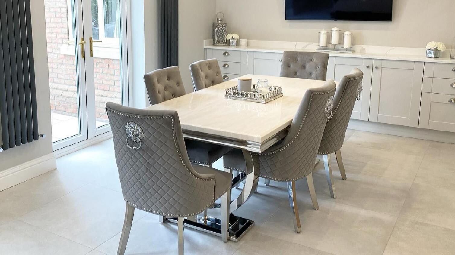 Grey dining room idea with a white table, grey velvet chairs, white tile floors, and light grey shaker base cupboards.