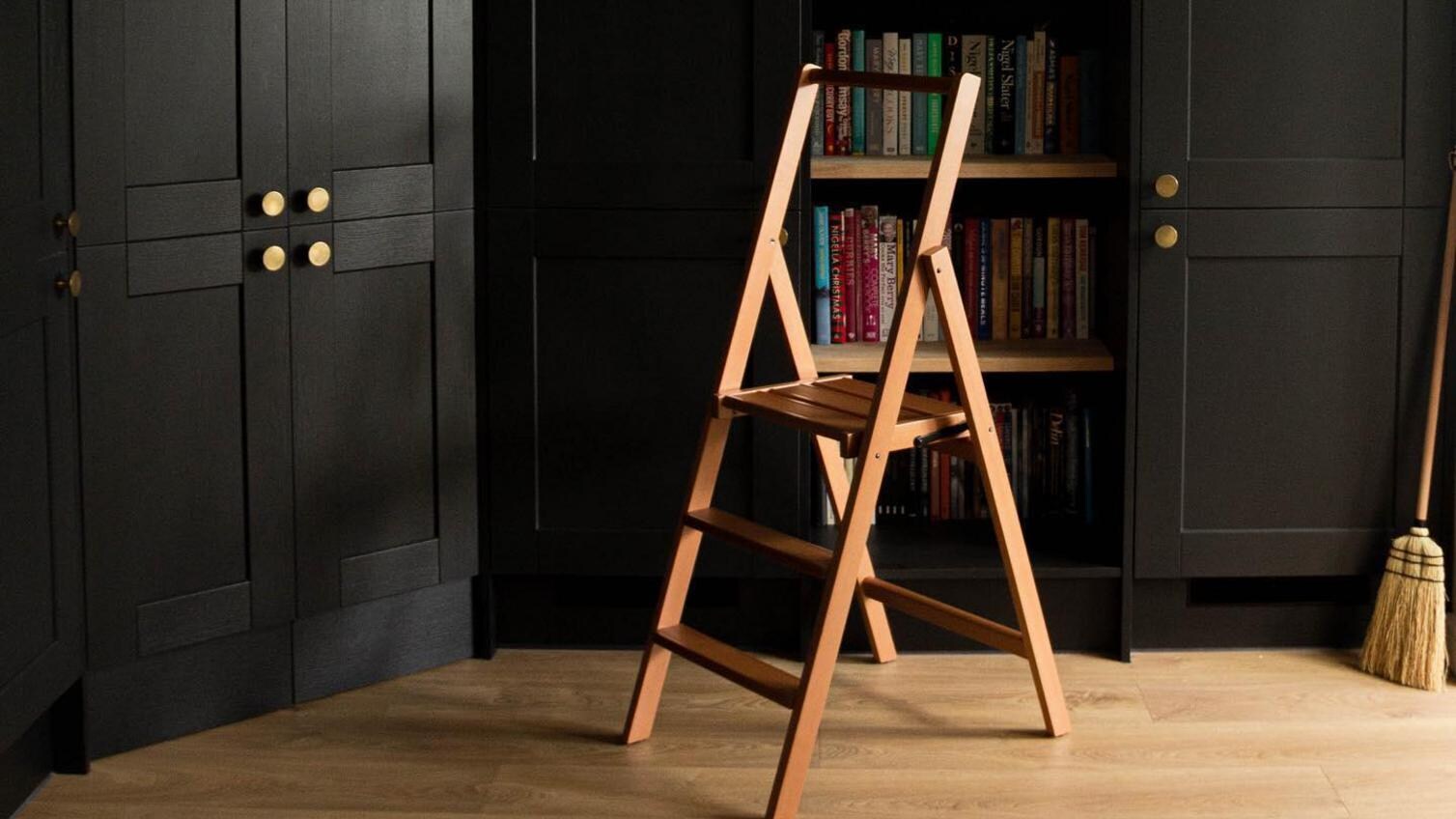 Black dining room idea with built-in tower cupboards, gold knob handles, a custom bookshelf, oak floors, and an oak ladder.