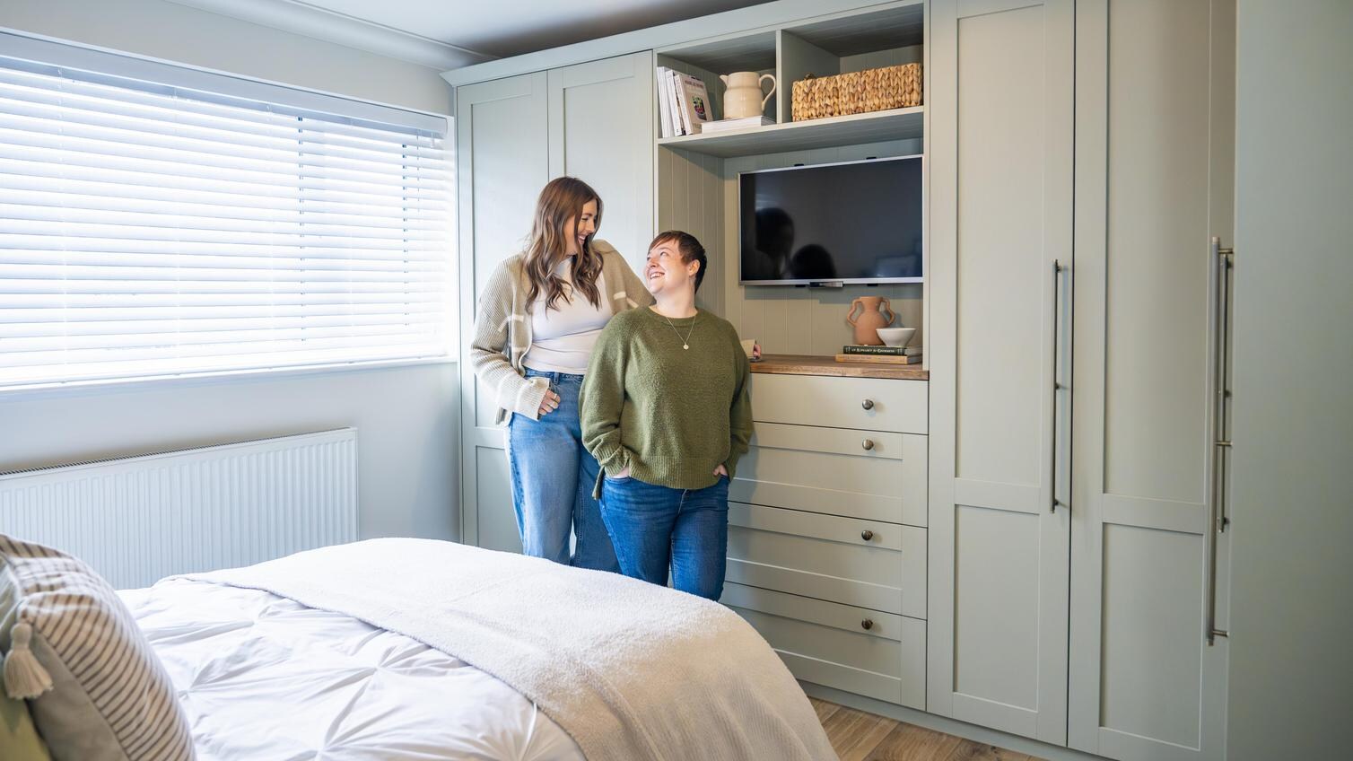 Rhiannon and Kayleigh stood in their Howdens bedroom, which is in a reed green colour from the Halesworth collection.