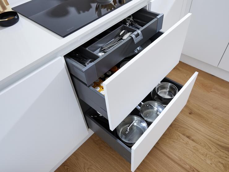 A compact white kitchen with two pan drawers and cutlery tray fitted beneath a black induction hob.