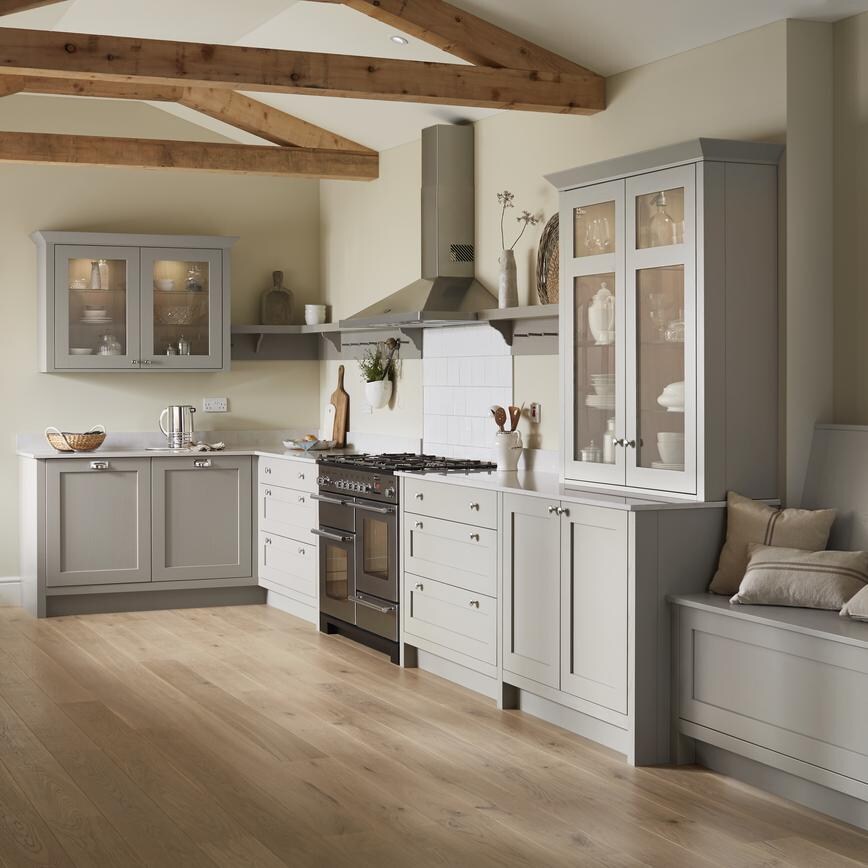 L shape kitchen in pebble grey with shaker style doors. Seated storage bench with cushions and worktop mounted glass cabinet.