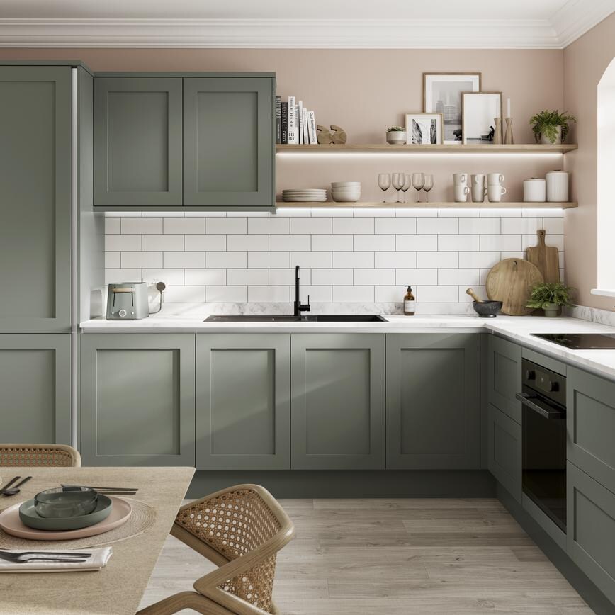 A reed green handleless kitchen idea in an l-shaped layout, with white worktops, black fixtures, and white backboard tiles.
