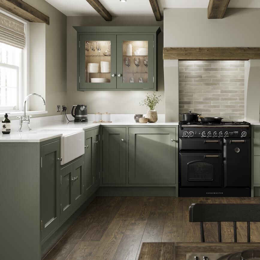 A reed green kitchen design in an open-plan layout with dark wood floors, shaker doors, a range cooker, and a ceramic sink.