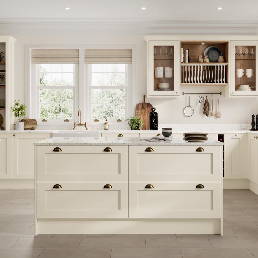 A cream-coloured, Linen shaker kitchen in an island layout. It has brass accessories, quartz worktop, and tile flooring.