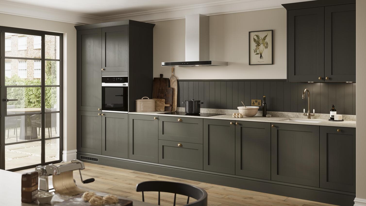 A deep green shaker kitchen with metallic handles. Finished with grey worktop, oak plank flooring, and built-in oven. 