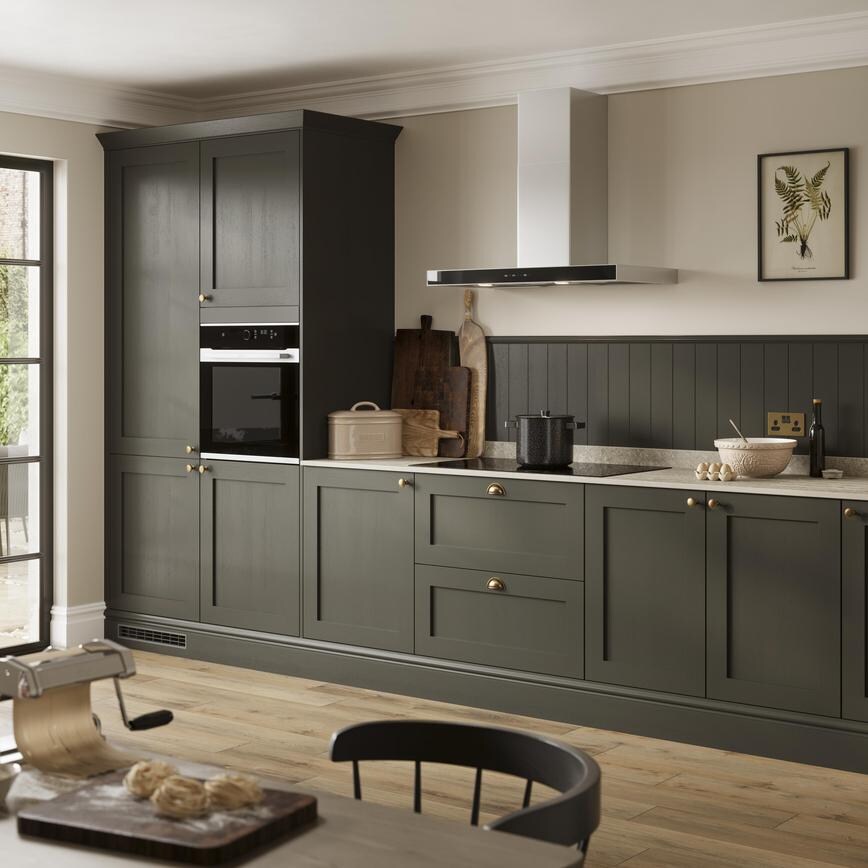 A deep green shaker kitchen with metallic handles. Finished with grey worktop, oak plank flooring, and built-in oven. 