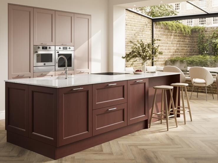 A two-tone, dark-red and light pink kitchen in an island layout. It has herringbone flooring and white worktops.