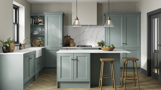 An l-shaped shaker kitchen, with a seafoam blue finish. It has a kitchen island, brass accessories, and oak-style flooring.