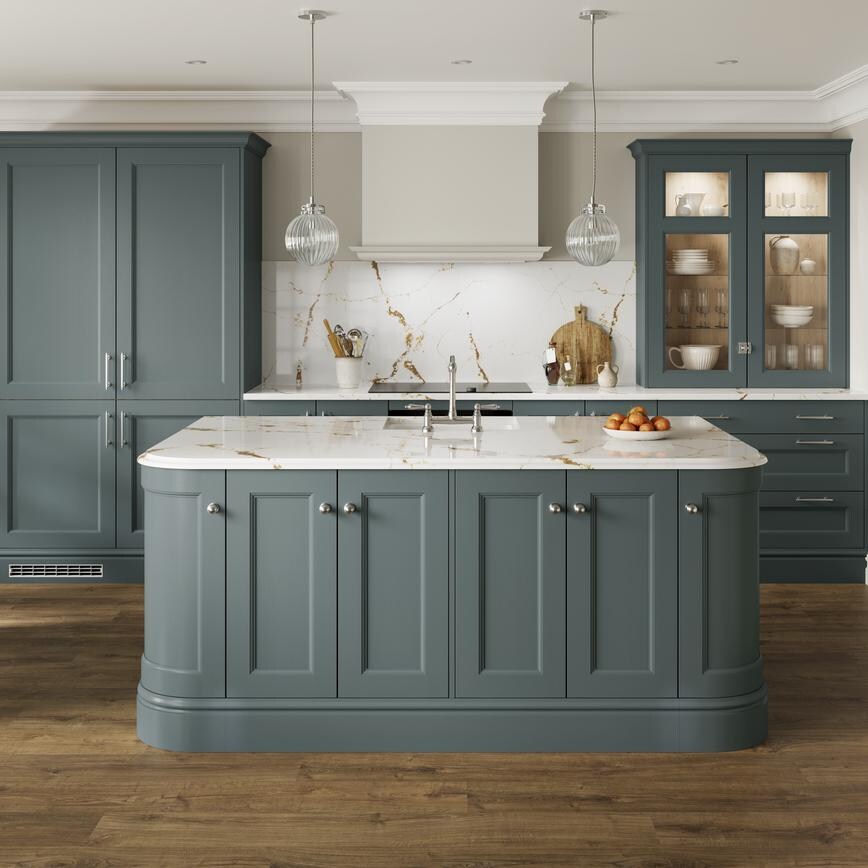 A light blue shaker kitchen in a single wall and island layout. It is finished with white worktops and oak flooring