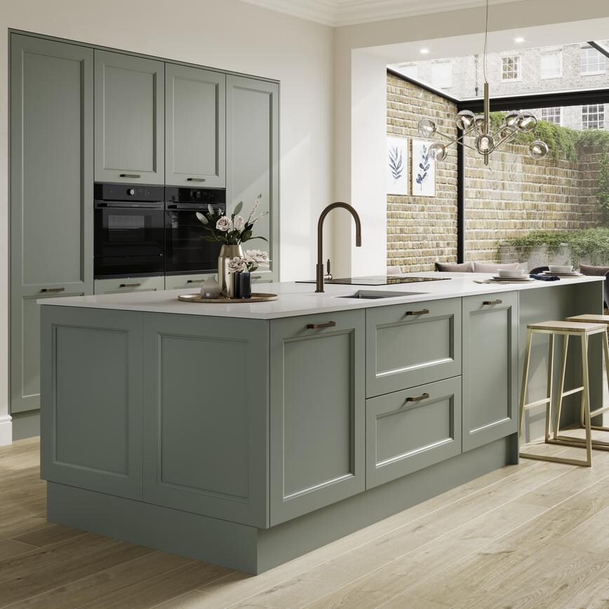 A reed green shaker kitchen in a single wall and island layout. There are black accessories, appliances, and wood floors.