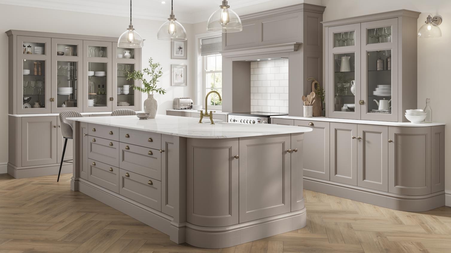 A mushroom-toned, brown kitchen with an island. It has white, bespoke worktop, brass handles, and curved cabinet doors.