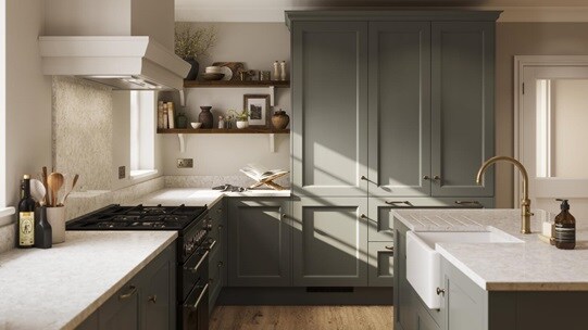 A green kitchen with shaker doors in an island layout. It has beige worktops, dark timber shelving, and plank flooring.