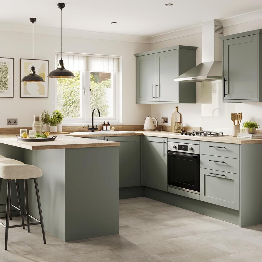 A light, reed green kitchen with shaker doors and bar handles. It is in a U-shaped layout and has timber worktops.