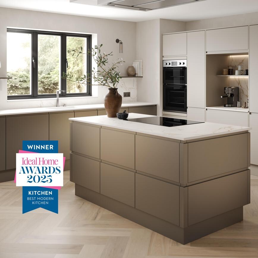 A handleless, bronze kitchen in an L-shaped, island layout. It has white worktops, chevron flooring, and an induction hob.