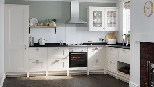 Classic cream shaker kitchen idea with ivory shaker doors in an L-shaped layout. Has silver cup handles and a built-in oven.