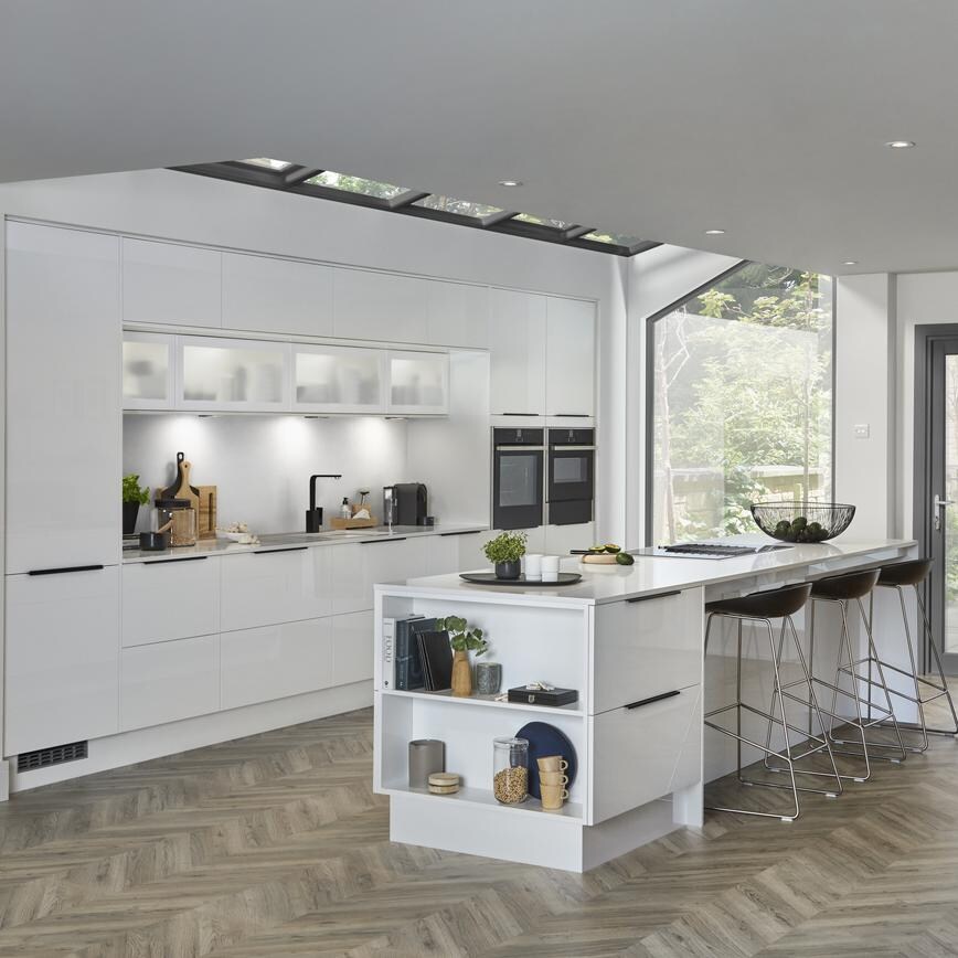 Modern white mirror gloss kitchen with two built in single oven and island unit with breakfast bar and open end shelving.