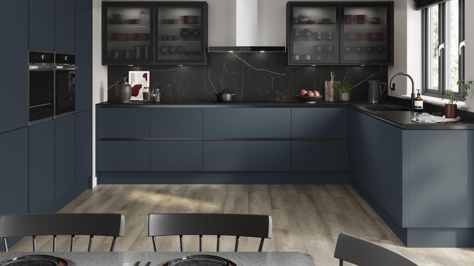 A marine blue handleless kitchen idea in a u-shaped layout. Has black profiles, fluted glass cupboards, and black worktops.