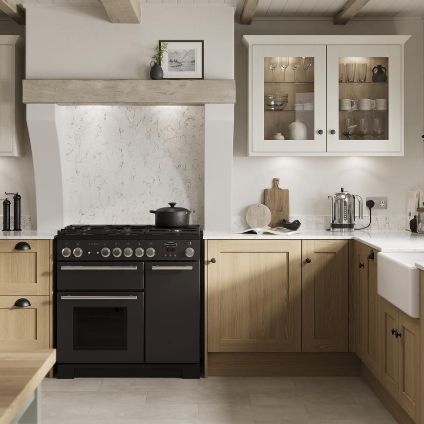 An L-shape kitchen with oak doors in a shaker style. Has white worktops and grey, tile-effect floors, and a black cooker.