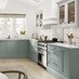 A blue kitchen idea with seafoam shaker cupboards. Contains white worktops, timber floors, and a double-bowl butler sink.