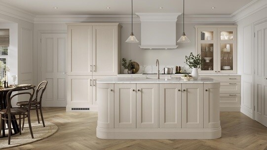 A cream, linen kitchen with shaker cabinets and glass doors. There is an island with curved corners and white worktop.