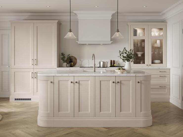 A cream, linen kitchen with shaker cabinets and glass doors. There is an island with curved corners and white worktop.