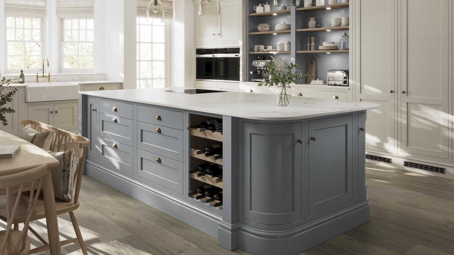 A blue shaker kitchen from Ilfracombe Dusk Blue, in an island layout with oak flooring. There is a run of linen-coloured cabinets