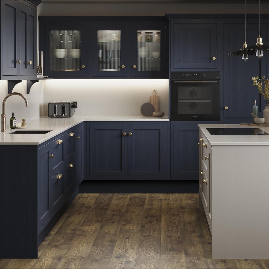 A navy shaker kitchen from Ilfracombe, in an l-shaped layout and a pebble-toned island. It also has dark oak flooring. 