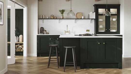 A green shaker kitchen from Ilfracombe Fir Green. It has a kitchen island, glass cabinets, and marble-style worktops.