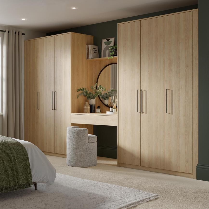 A bedroom with pale oak wardrobers and drawers. They have a visible textured finish and there is a fitted dresser between.