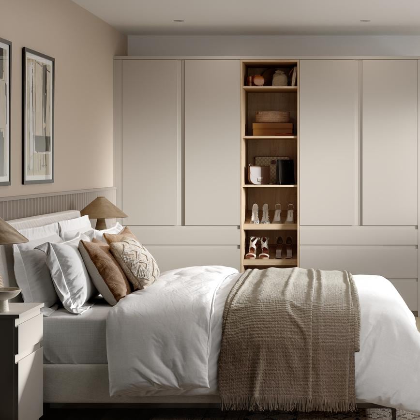 A matt sandstone bedroom with tall wardrobes and matching drawers. It has shelves in between and light, oak-style flooring.