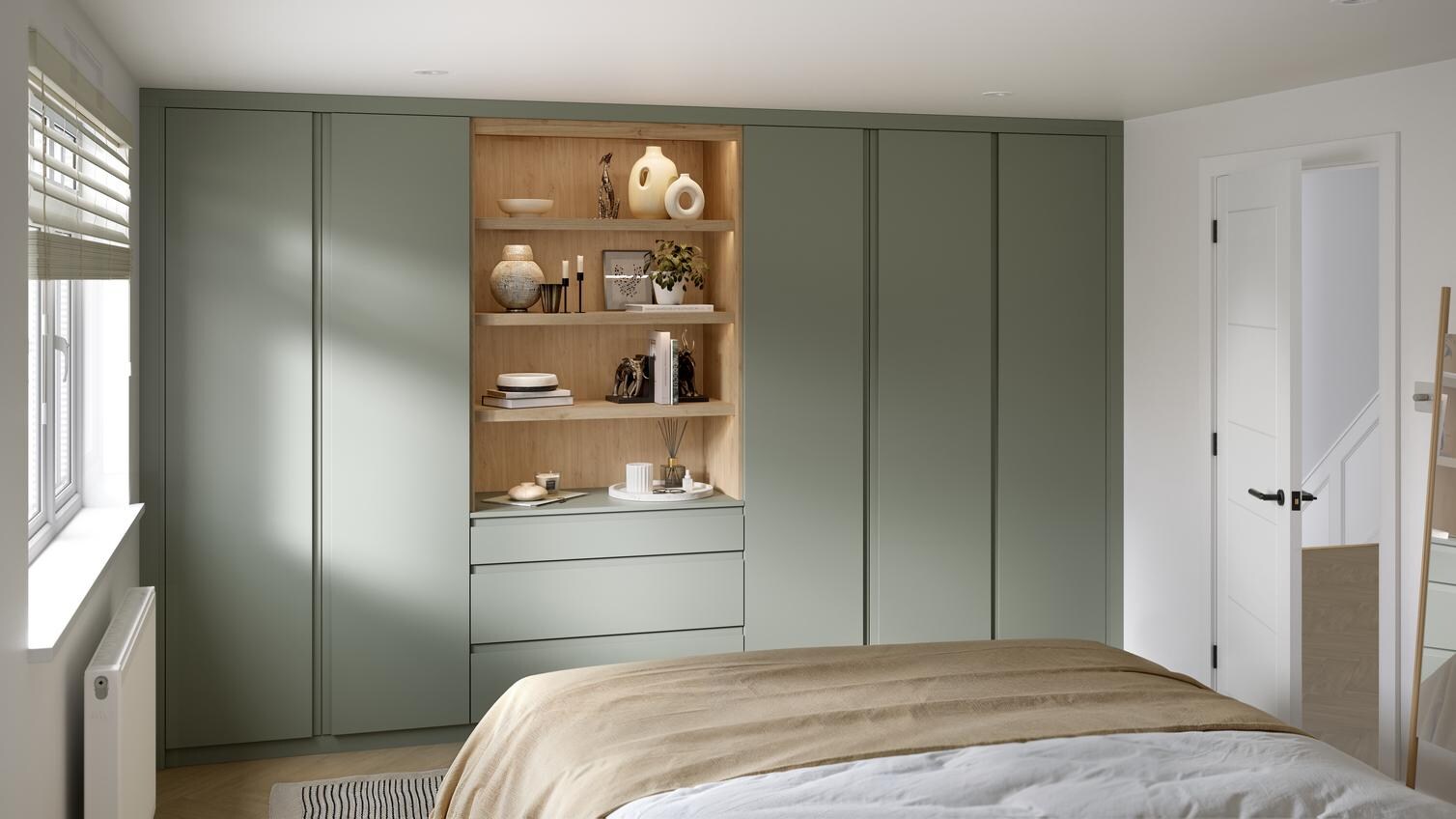 A Clerkenwell bedroom with reed green wardrobes & dressers, in a matt finish. There is oak shelving with drawers & lighting.