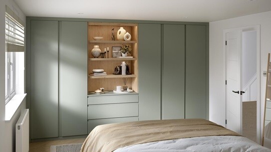 A Clerkenwell bedroom with reed green wardrobes & dressers, in a matt finish. There is oak shelving with drawers & lighting.