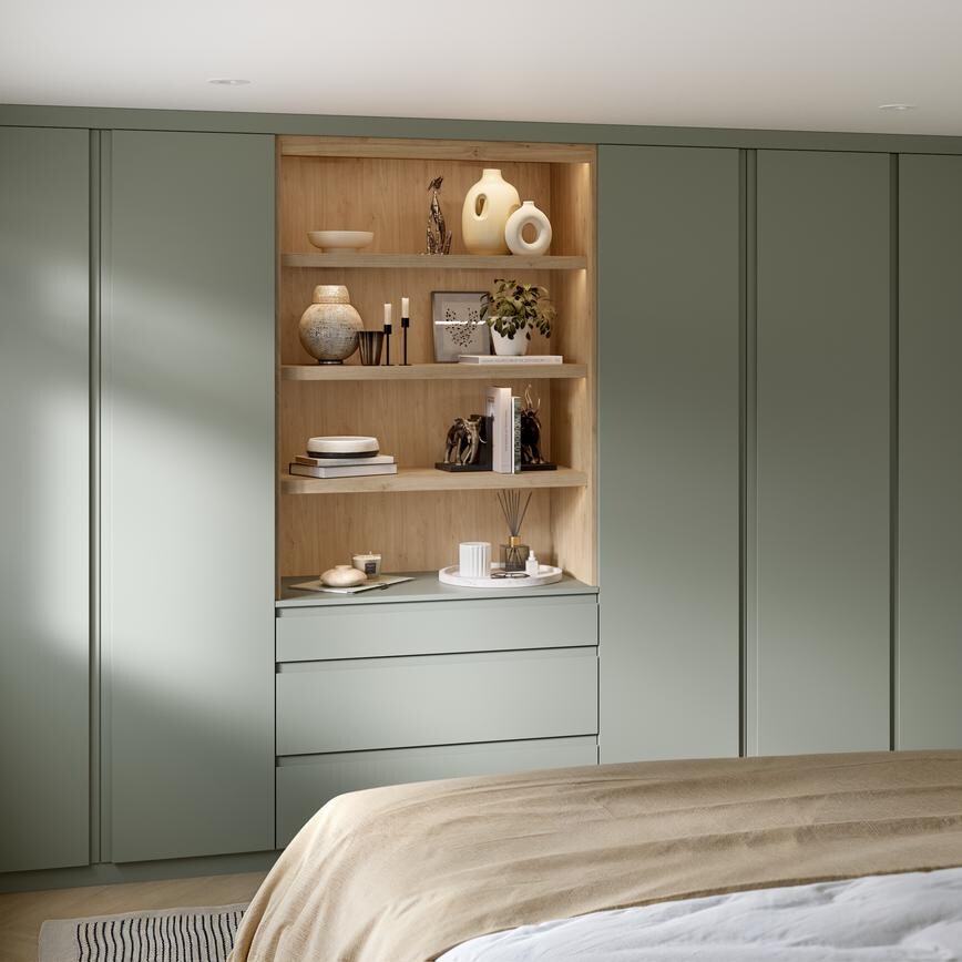 A Clerkenwell bedroom with reed green wardrobes & dressers, in a matt finish. There is oak shelving with drawers & lighting.