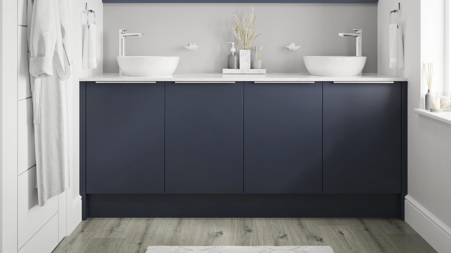 Small bathroom with navy base cabinets and trimline handles. Includes grey-oak flooring, white worktops and two white basins.