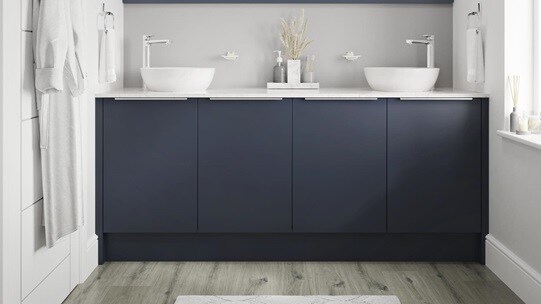 Small bathroom with navy base cabinets and trimline handles. Includes grey-oak flooring, white worktops and two white basins.