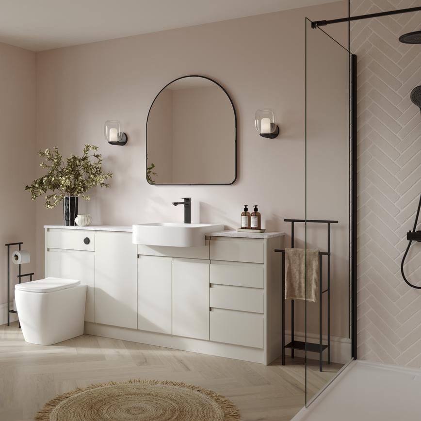 A white bathroom with porcelain-toned cabinets. It has herringbone oak flooring, glass shower panels, and black fixtures. 