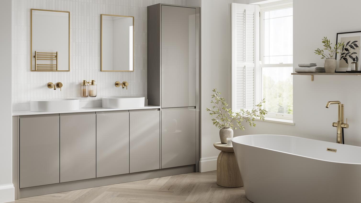 A bright bathroom with gloss, sand grey cabinets. It has oak-effect flooring, brass fixtures, and a large roll-top bath. 