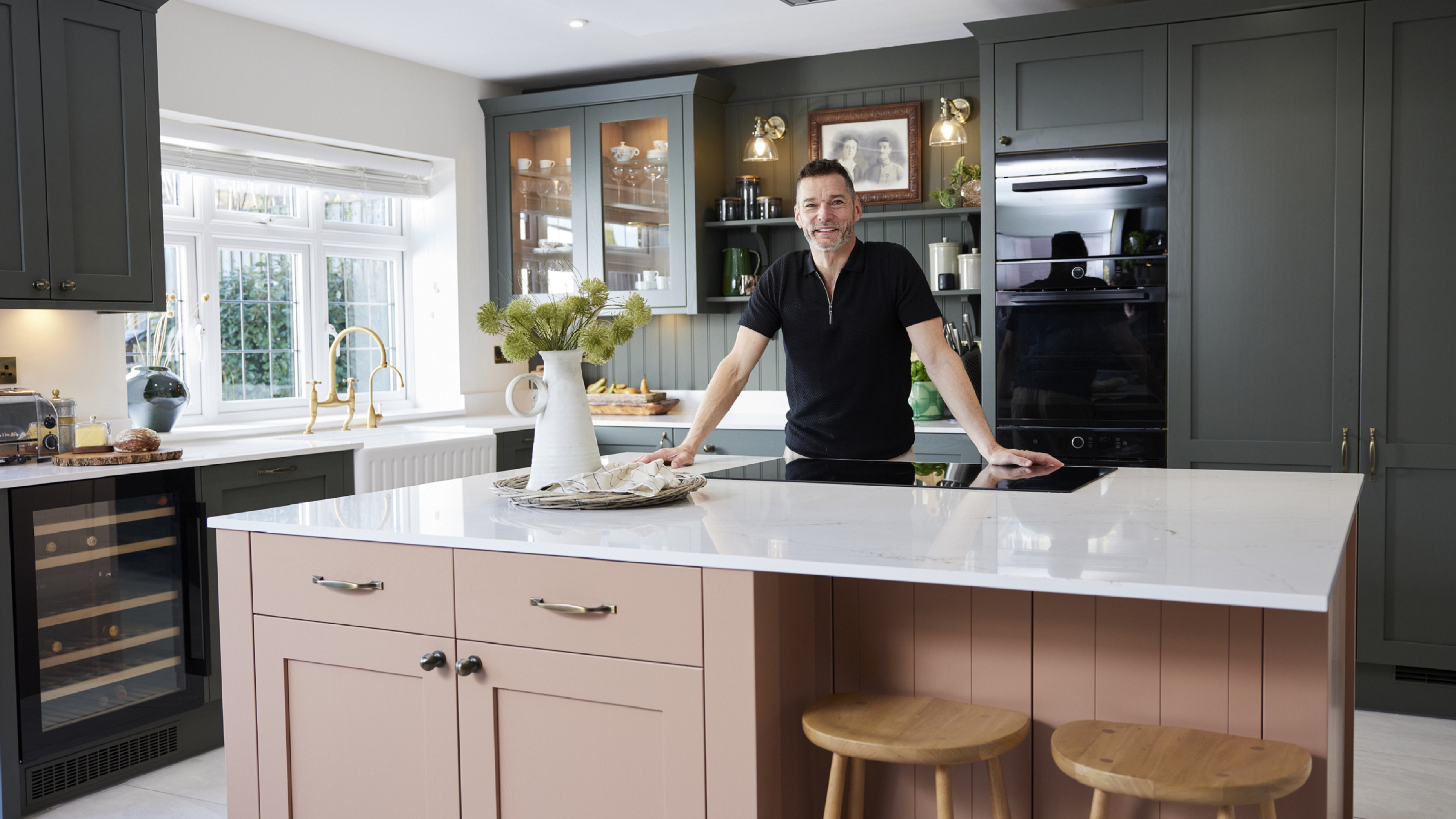 Fred Sirieix posing in his new Howdens kitchen, which has an ash green and terracotta colour scheme