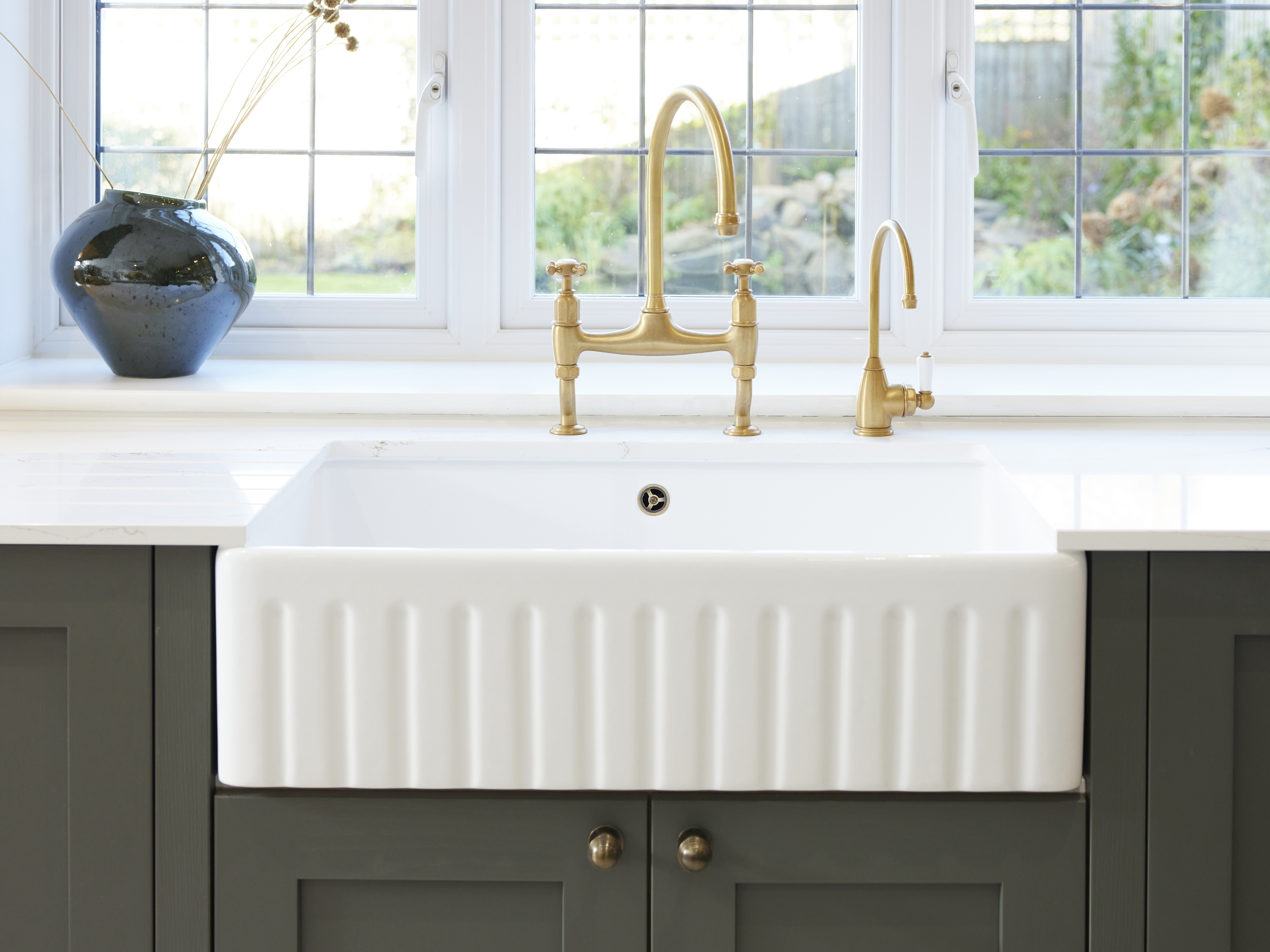 A white ceramic sink with a fluted design and golden taps