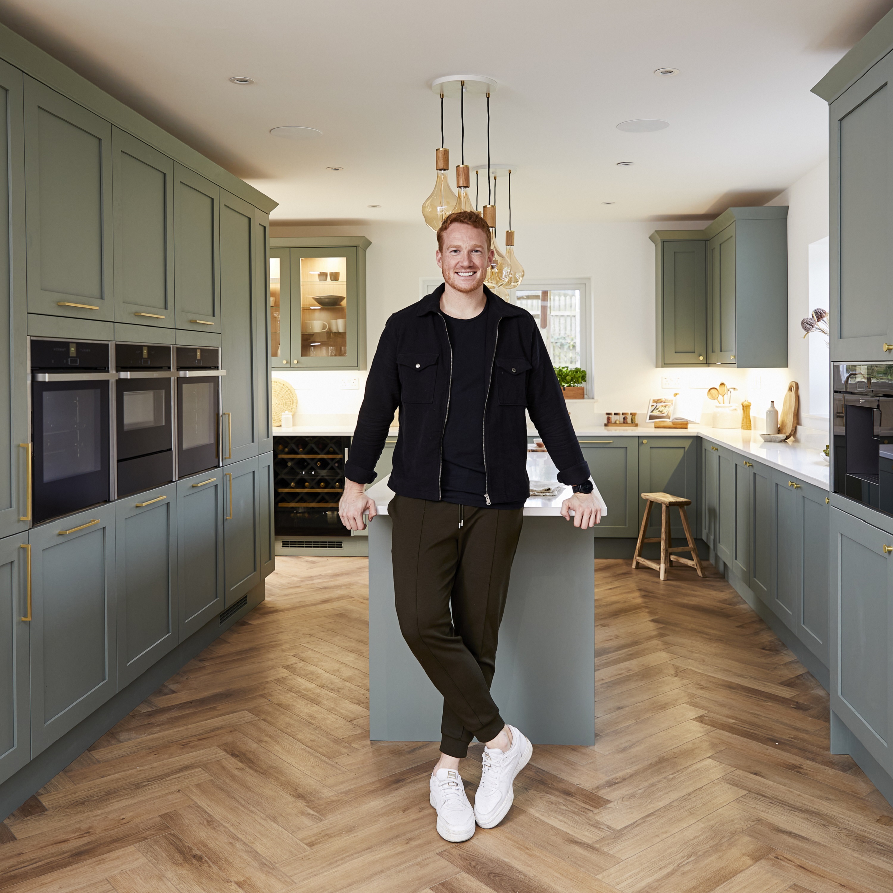 Greg leaning against the island in his new green kitchen